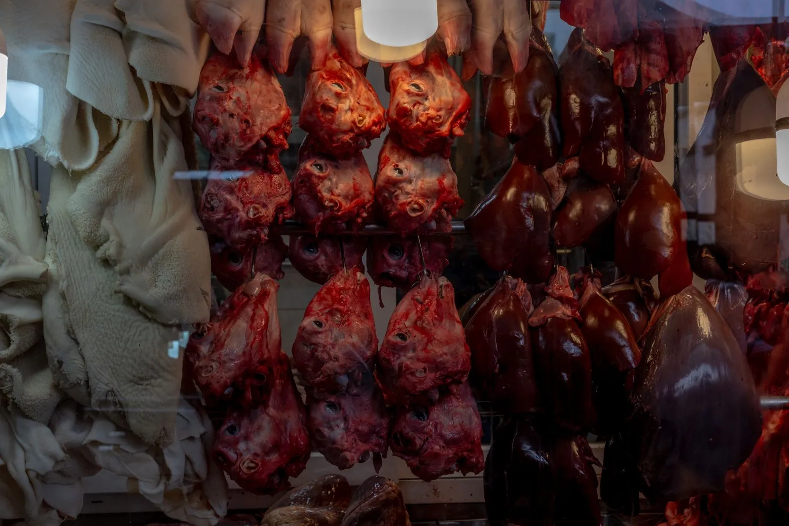 Close-up of various meat and organ cuts hanging in a butcher shop display window.