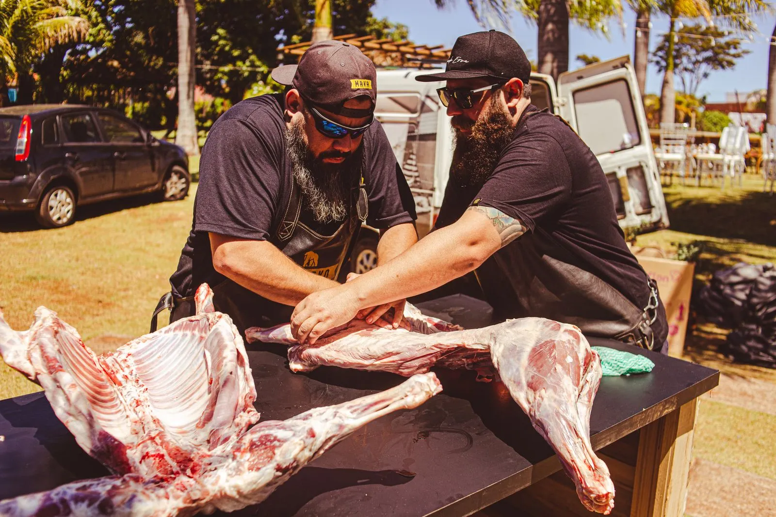 Two men butchering meat outdoors at a festival, showcasing traditional techniques.
